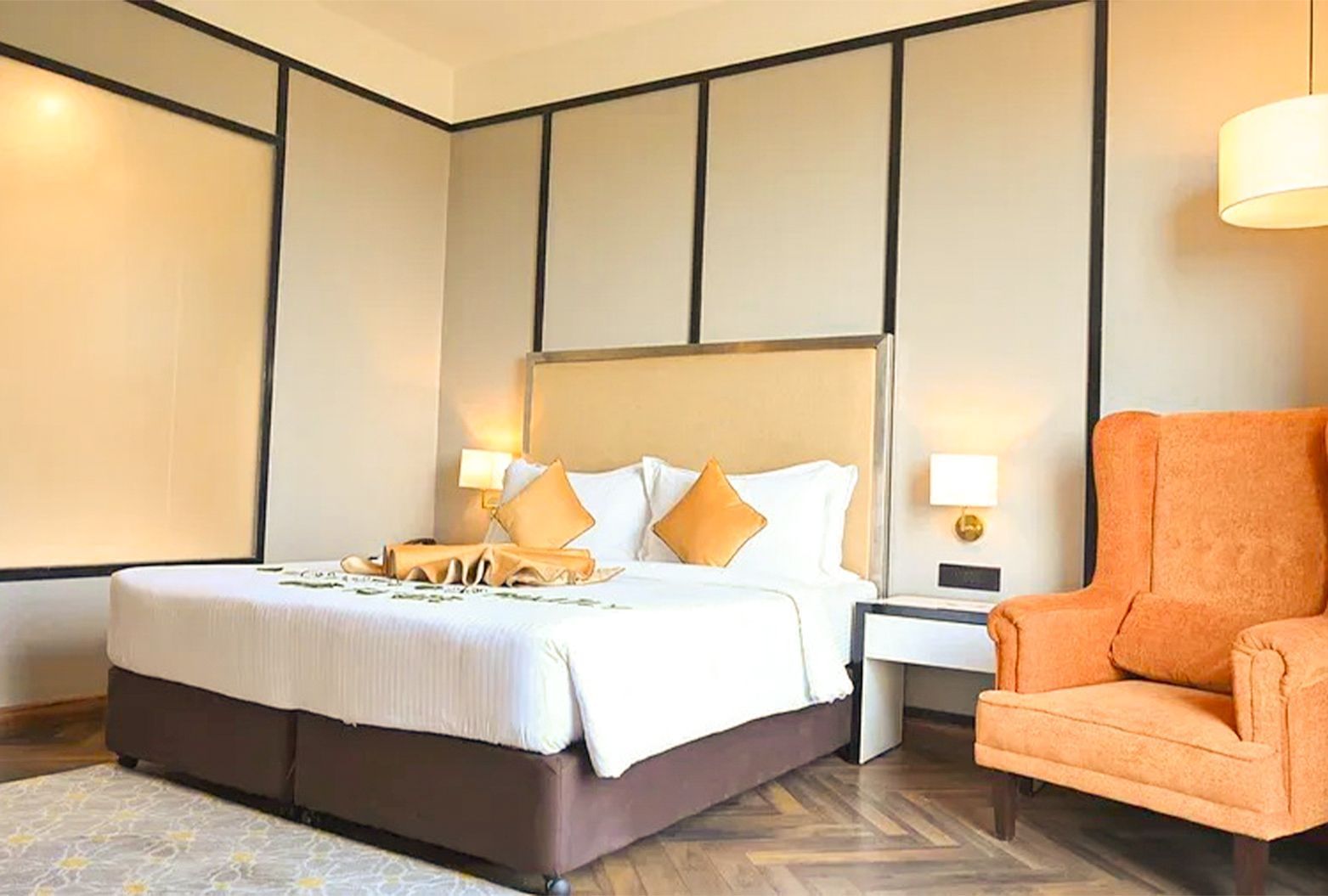 A low angle shot of a hotel bedroom featuring a king size bed and an orange couch - Polo Hotel Agartala