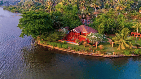 An aerial view of a resort cottage with a red roof nestled on a lush, green peninsula in a lake or backwater.