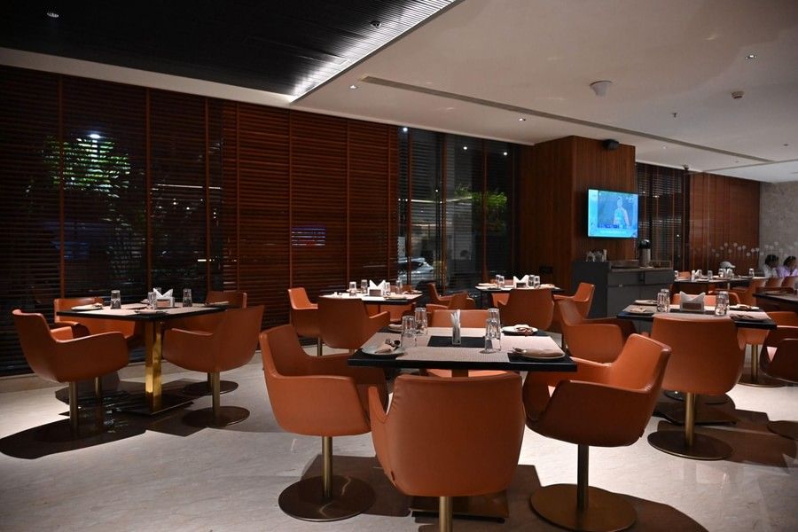 A contemporary dining area with round tables and orange chairs set against a warm, wooden backdrop.