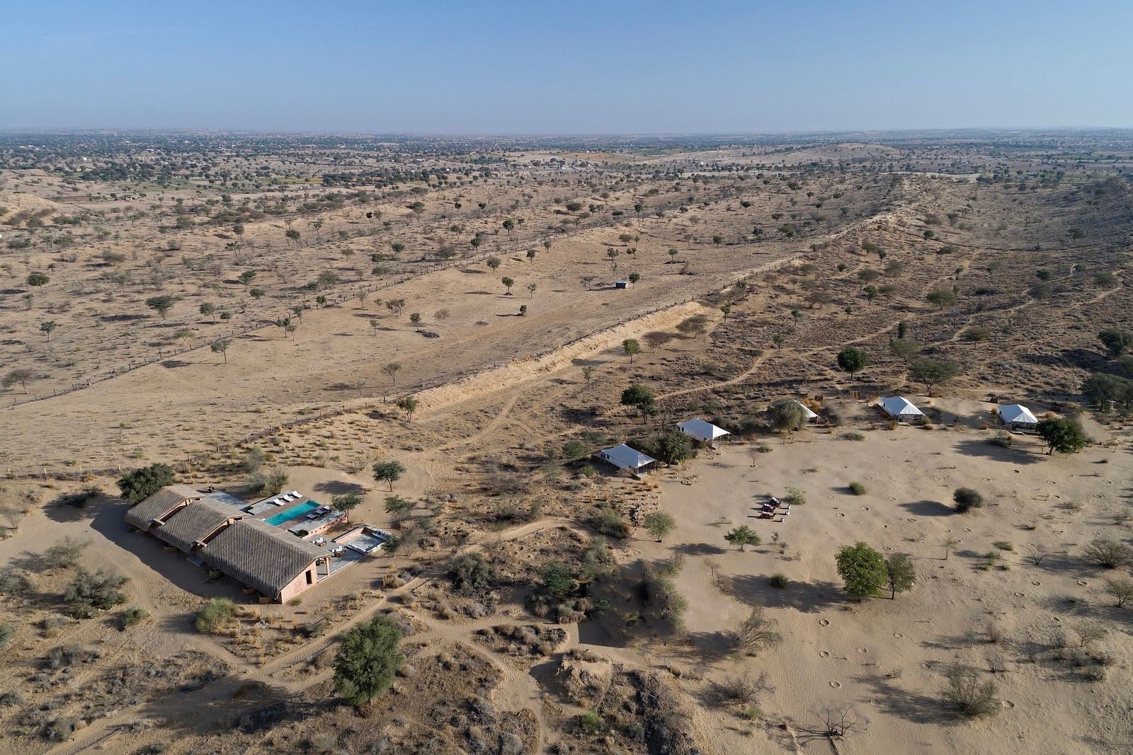 A luxury desert tent with an extended canopy stands amid a dry landscape with sparse trees, under a clear sky - MANVAR Resort & Desert Camp