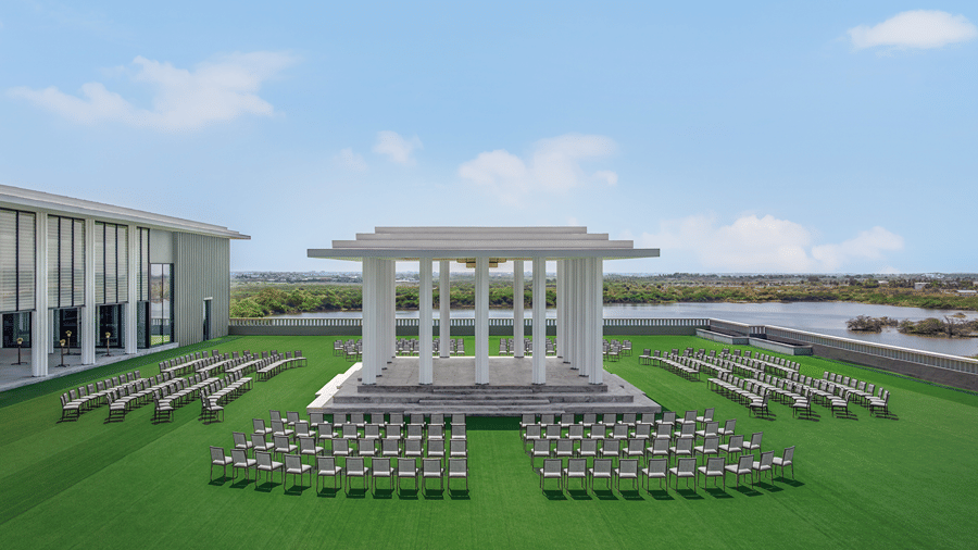 Rooftop Mandapam with rows of chairs facing a white pillared pavilion on green turf, overlooking a lake under a blue sky, at The Residency Signature Madurai.