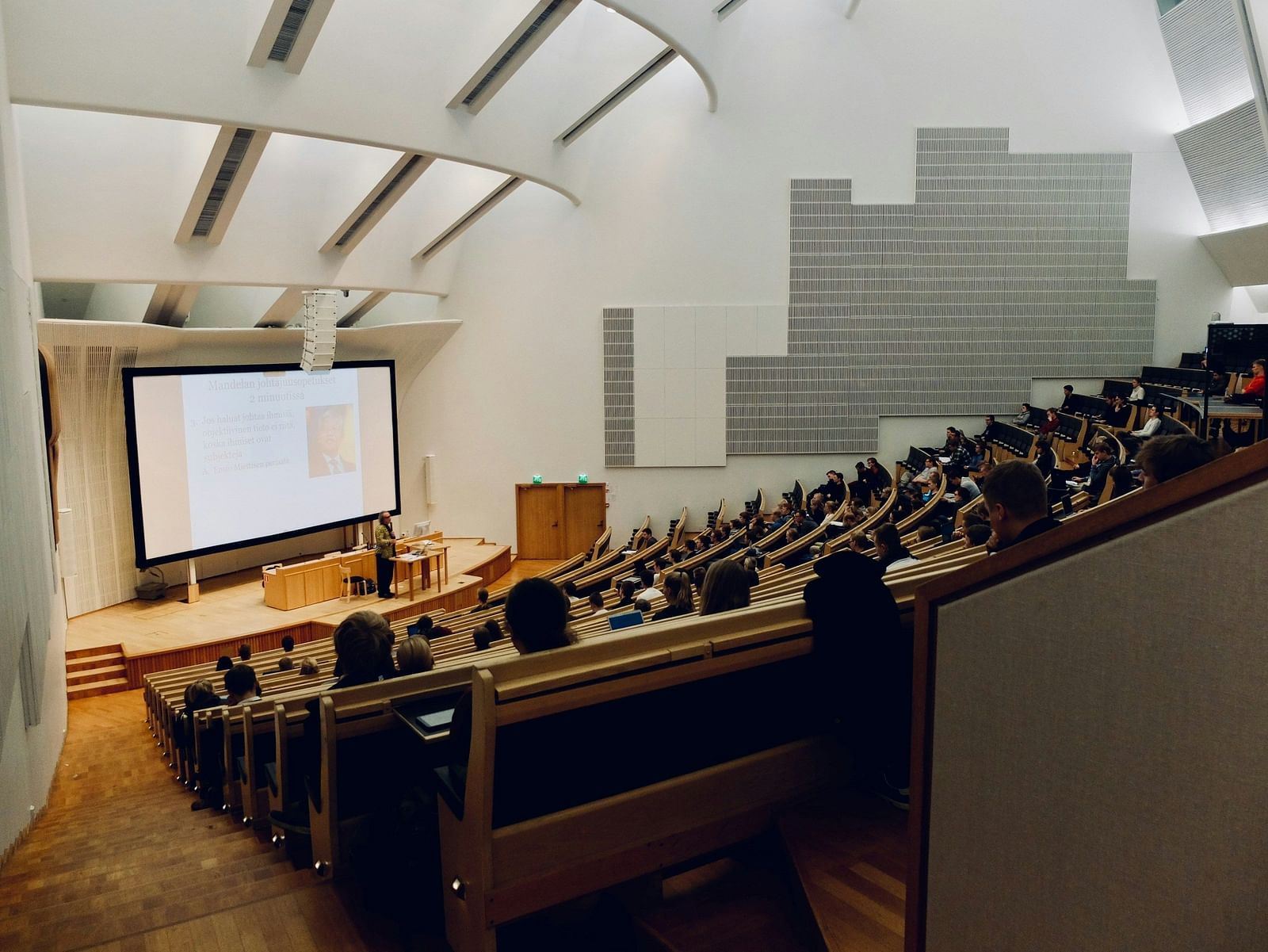 An overview of a classroom as seen from the top with a large screen and a teacher's desk at the bottom.