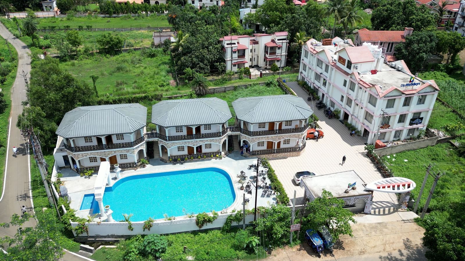 Aerial view of Dip Holidays featuring cosy cottages, a large outdoor swimming pool, and lush green surroundings.