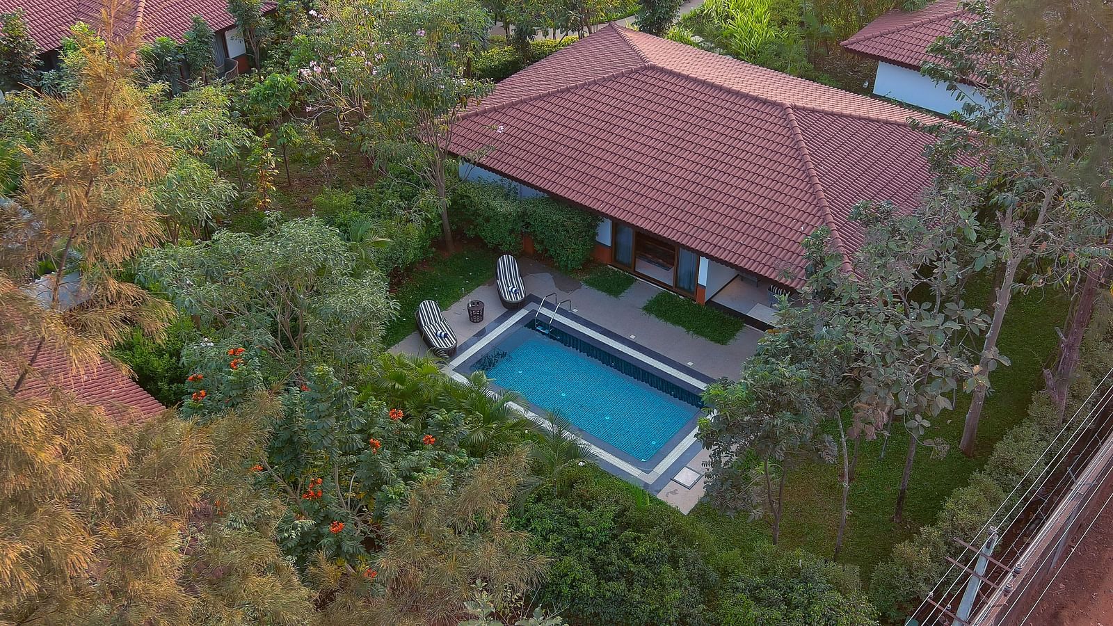Aerial shot of Gamyam Retreat with a terracotta roof, surrounded by trees, and a rectangular blue swimming pool.