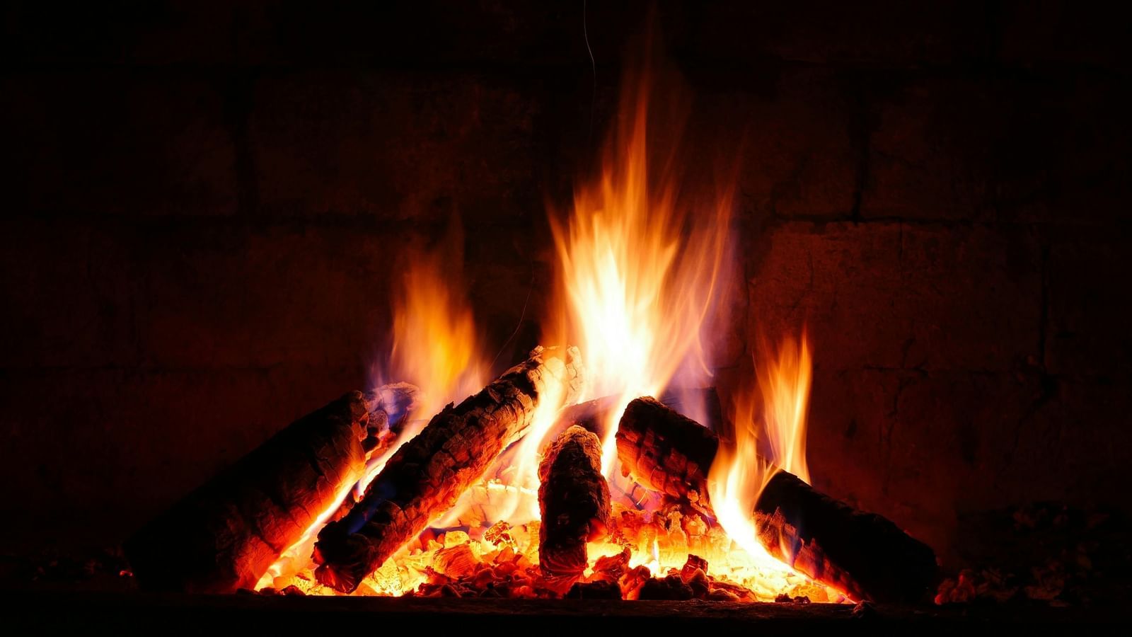A close-up shot of a roaring fire in a dark fireplace, with bright orange and red flames.