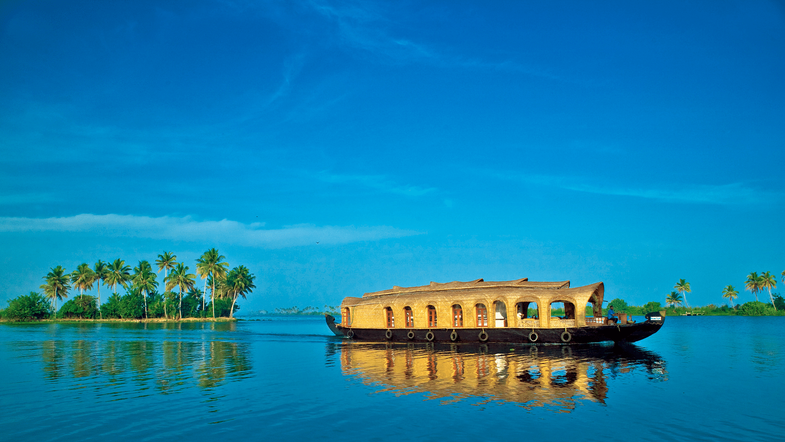 an image of Houseboat on blue lake waters with trees in the background - Rhythm Kumarakom