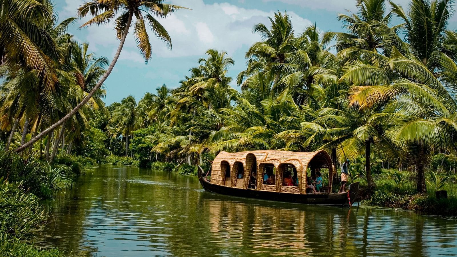 House boat going through a water body surrounded by lush greenery