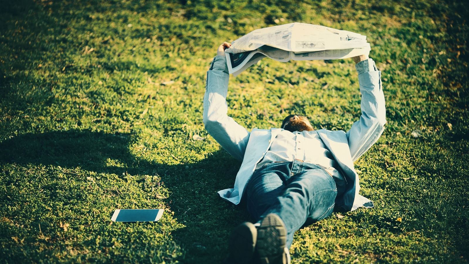 an image of Man lying on grass reading newspaper - Rhythm Lonavala