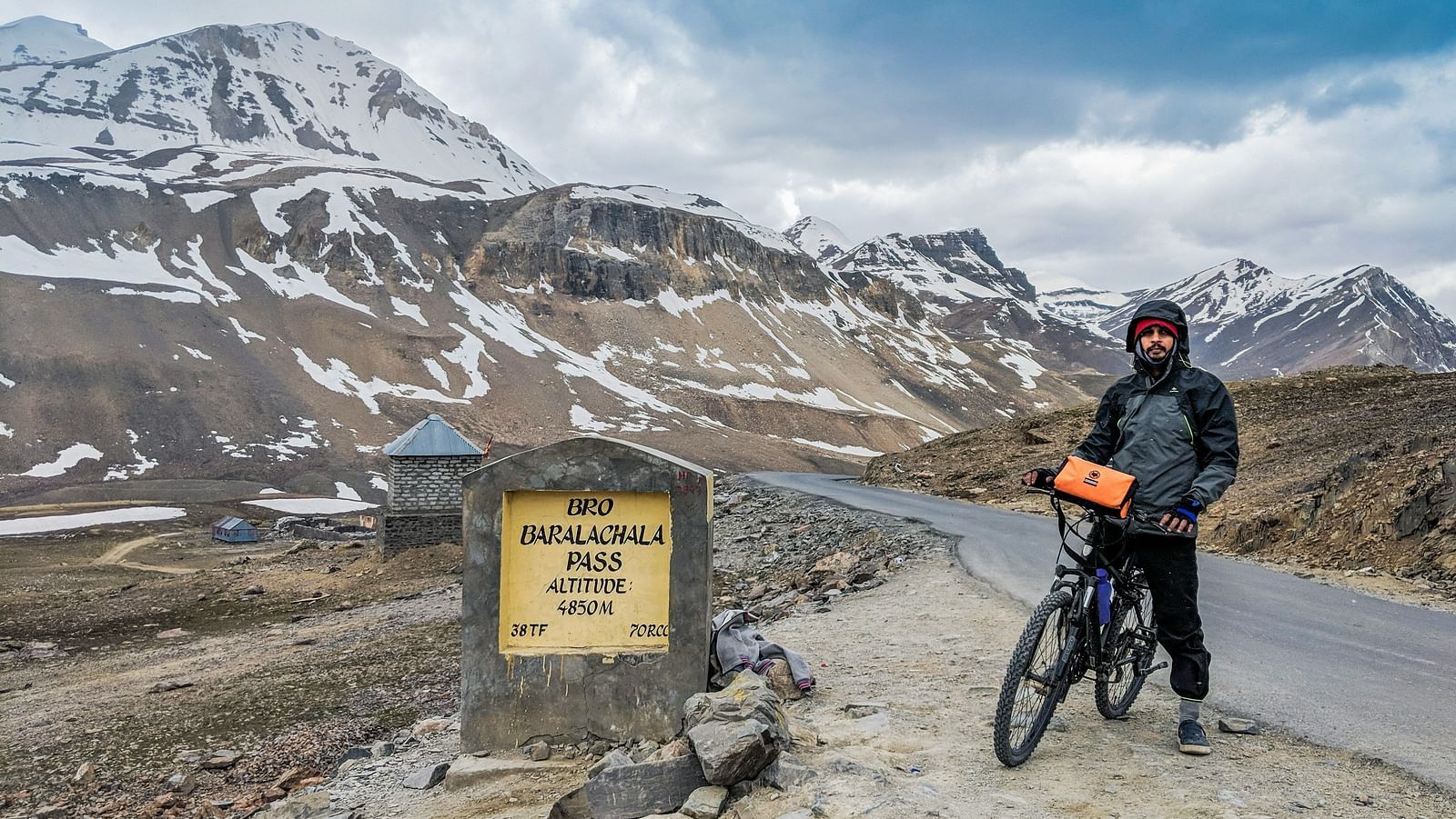 A biker posing with their bicycle at a high-altitude road sign