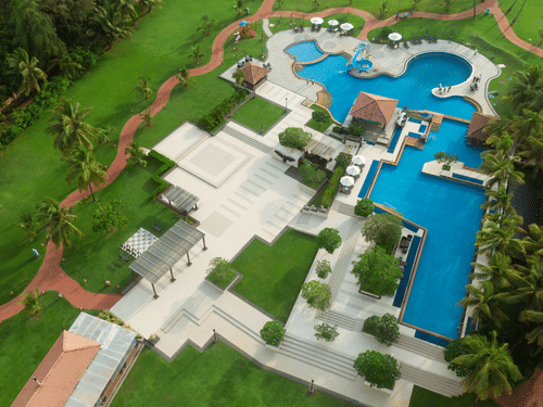 An aerial view of Kenilworth Resort & Spa, Goa, with the different rooms, lawn area, trees, walking pathway, and the swimming pool in view.
