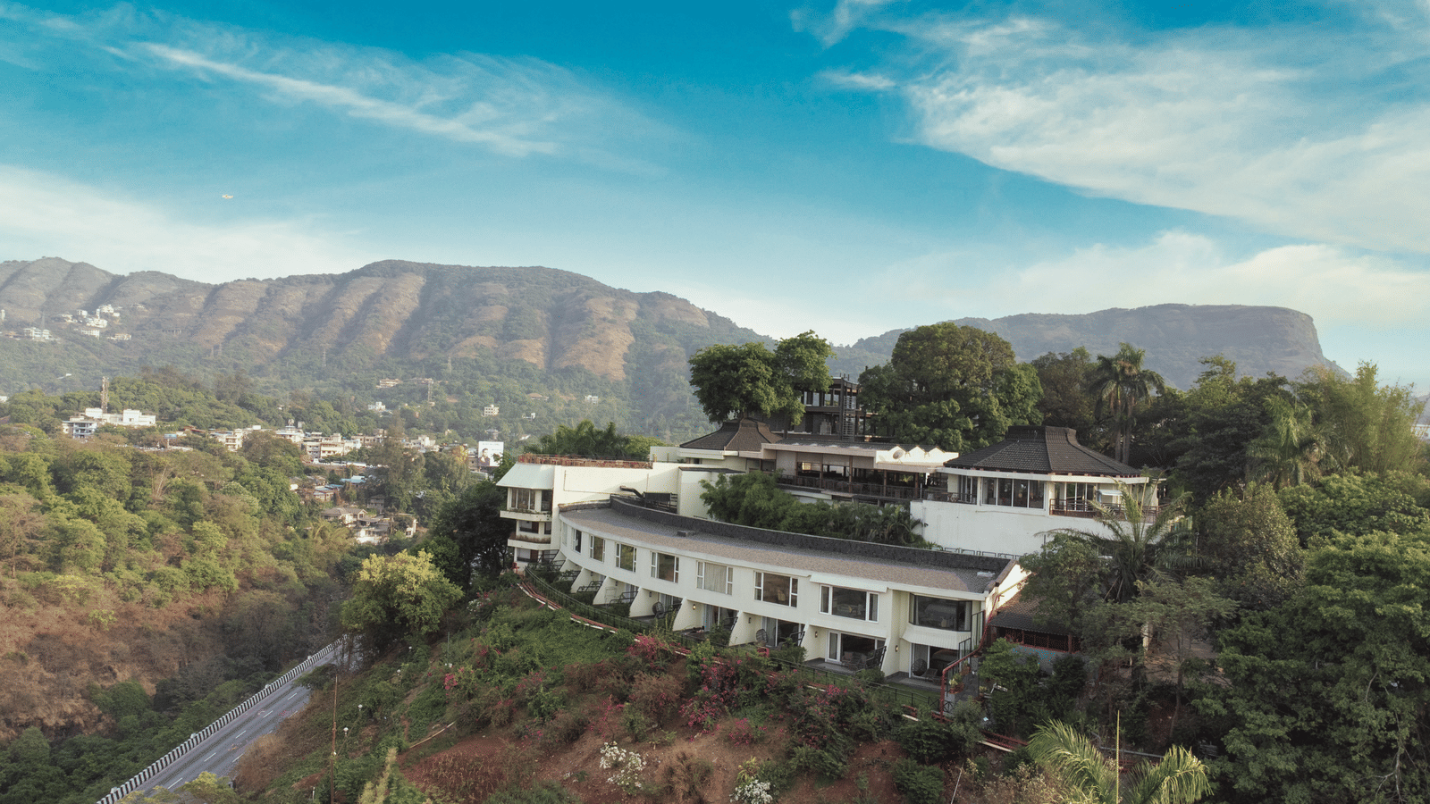 An exterior view of Athiva Hotels & Resorts, set on a hill under a bright sky and distant mountains.