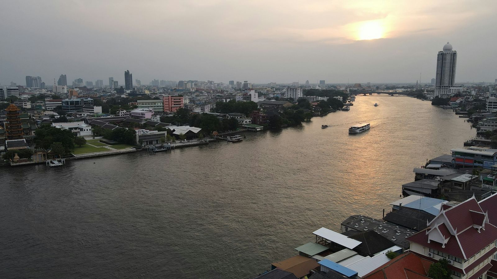 An aerial view of Chao Phraya River with a cruise on it and the sun setting in the background.