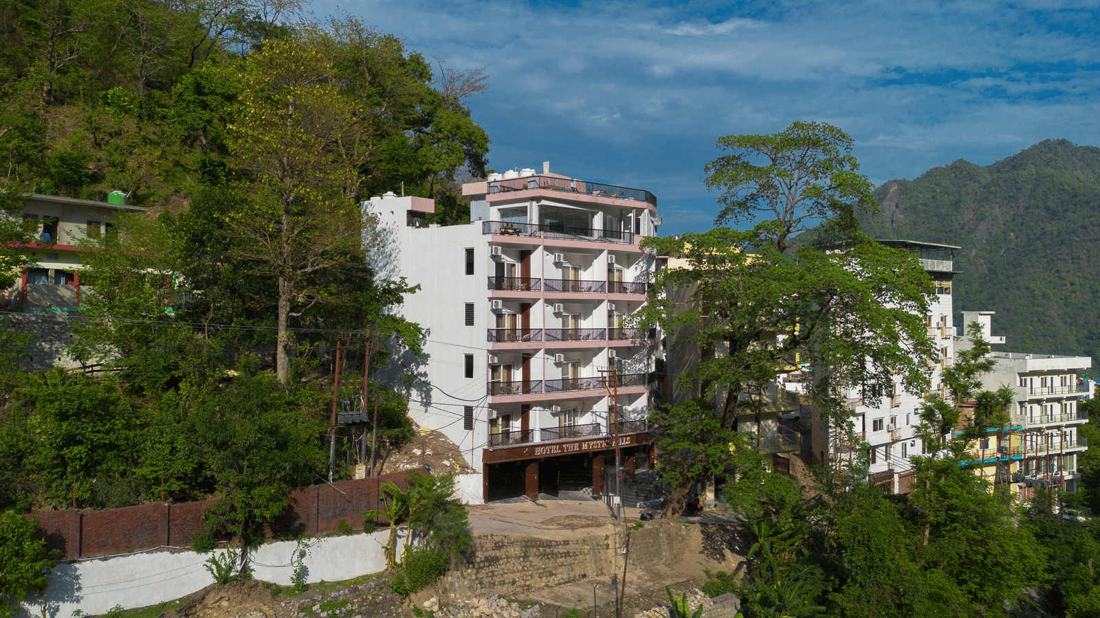An exterior of a building with multiple storeys, balconies, and windows, surrounded by trees on a hillside in Perfectstayz Premium Mystic Falls, Rishikesh.