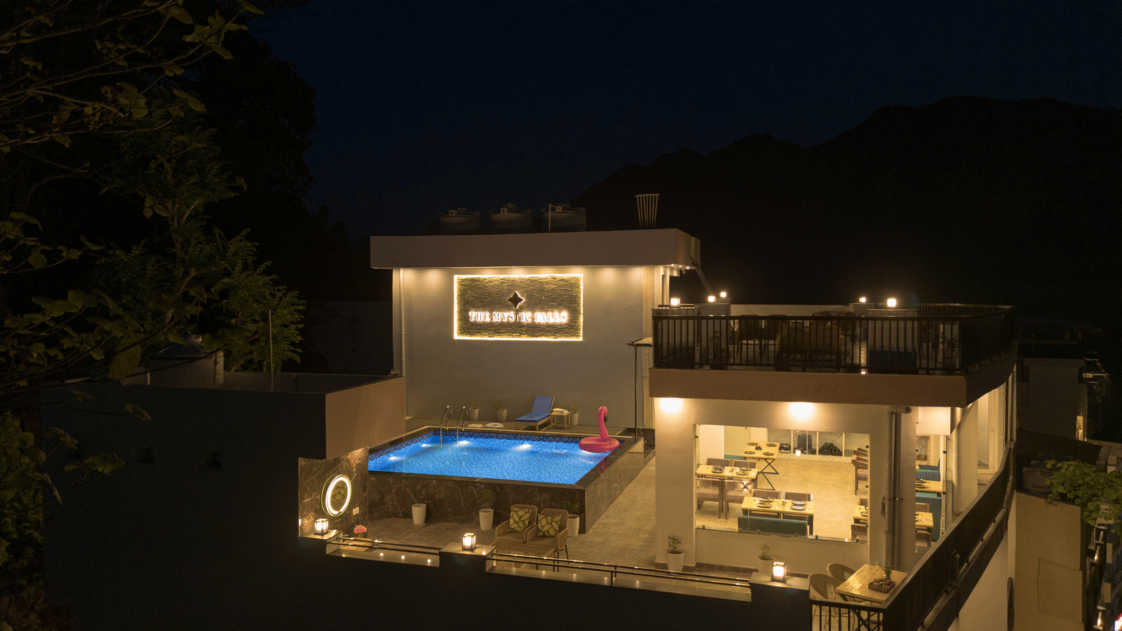 An exterior view of at night, showing a terrace area, lights, and a swimming pool in Perfectstayz Premium Mystic Falls, Rishikesh.