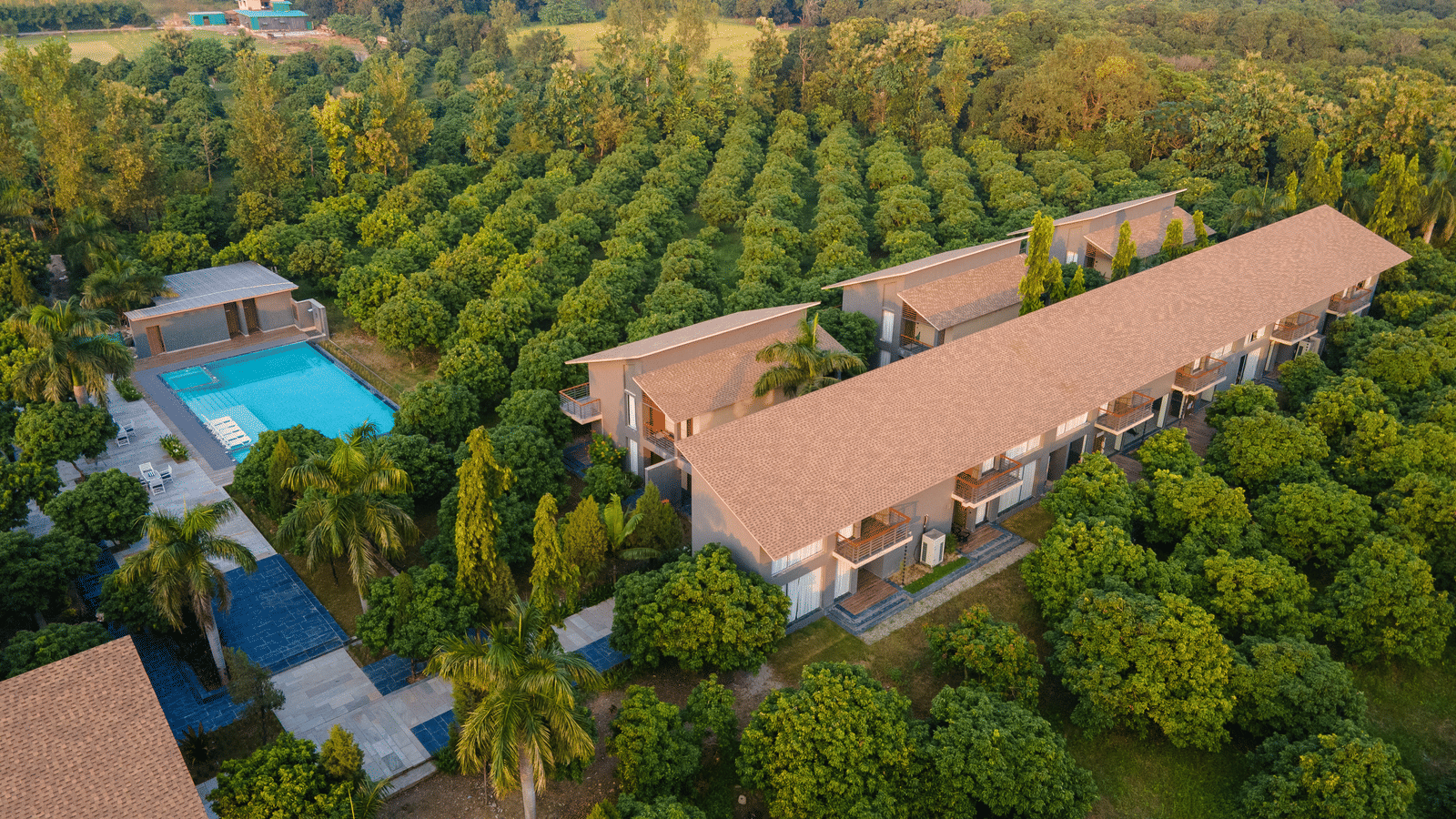 An elevated view at Wyndham Garden featuring a long low-rise building, a swimming pool area, and surrounded by a grove of small trees.