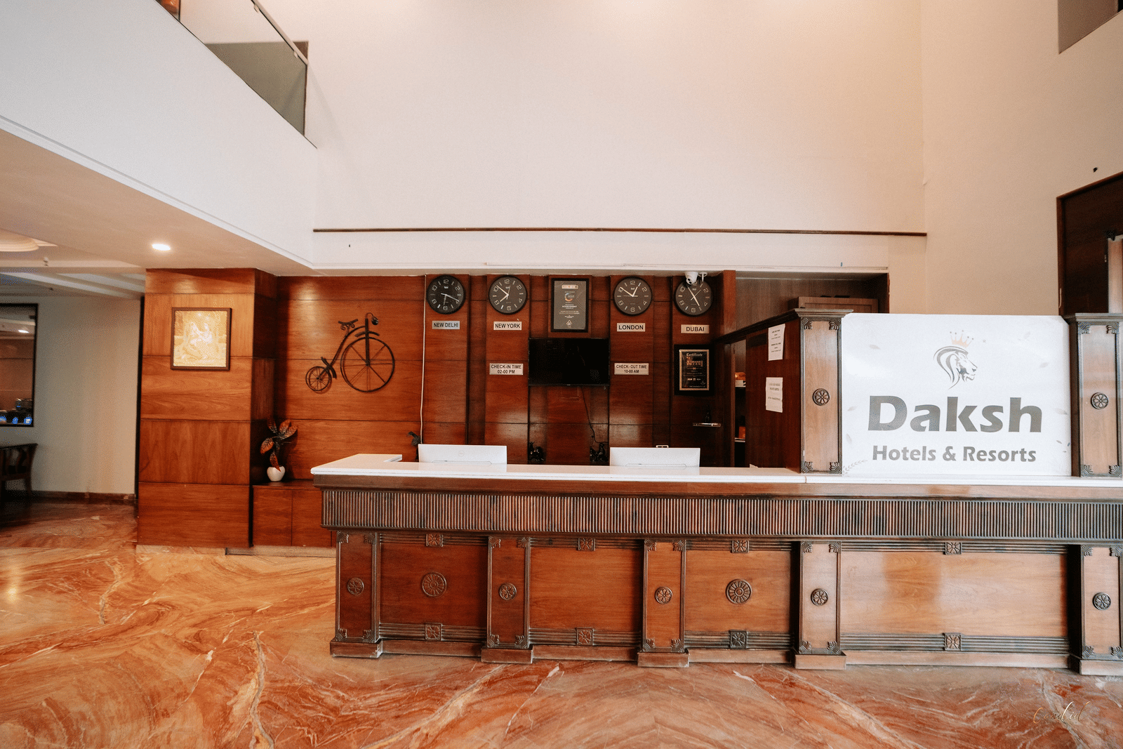 The hotel reception desk with a dark wood finish and a marble-effect floor at Daksh The Madhuvan Suites, Dwarka.