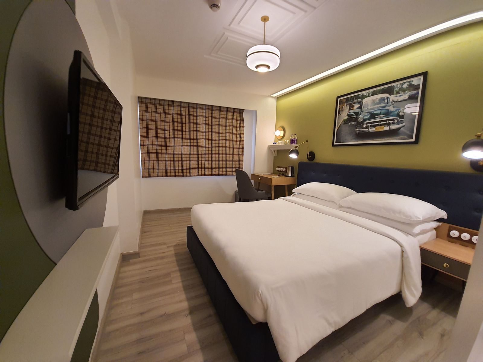 A modern and comfortable hotel room with a king size bed, a bedside table, a work desk with a chair, a  TV, and a window with curtains  | T24 Retro