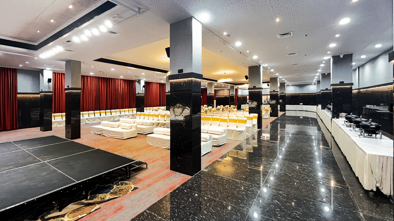 Spacious banquet hall with black marble floor, stage, and ceiling lights at Infiniti Hotel, Indore.