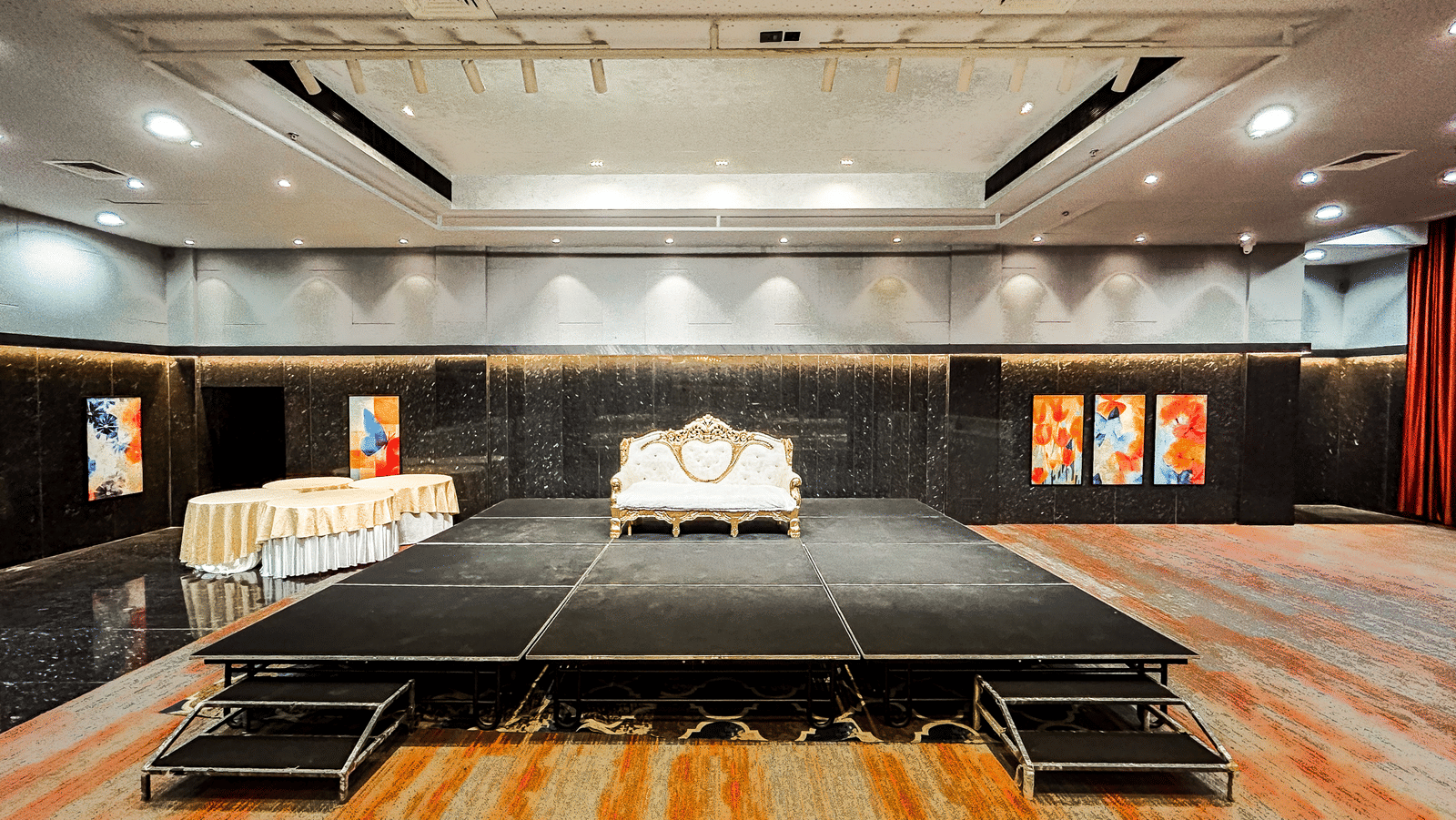 Carpeted banquet hall with a huge stage, ceiling lights, and wall decor at Infiniti Hotel, Indore.