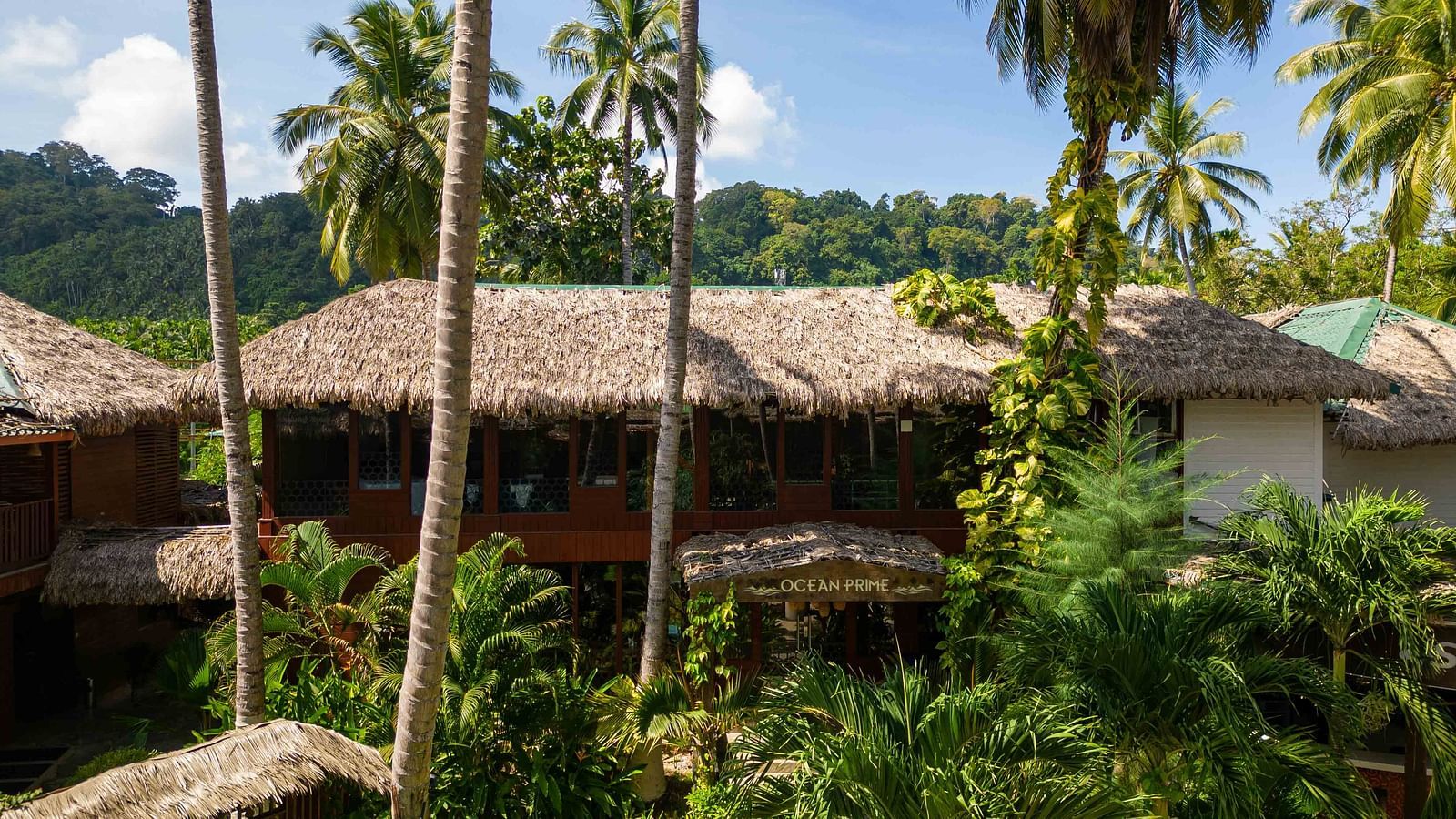 A view of a rustic building at Coral Reef Resort and Spa in Havelock with a thatched roof, nestled within the greenery. The building blends seamlessly with the natural surroundings, enhancing the tropical feel - Coral Reef Resort & Spa, Havelock