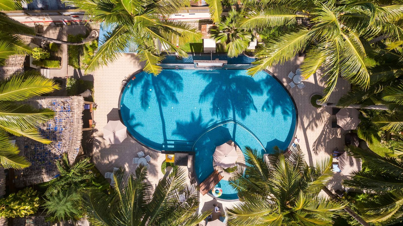  An aerial view of a pool with an intricate design, surrounded by lush foliage. The water in the pool creates a relaxing blue hue amidst the tropical garden - Coral Reef Resort & Spa, Havelock