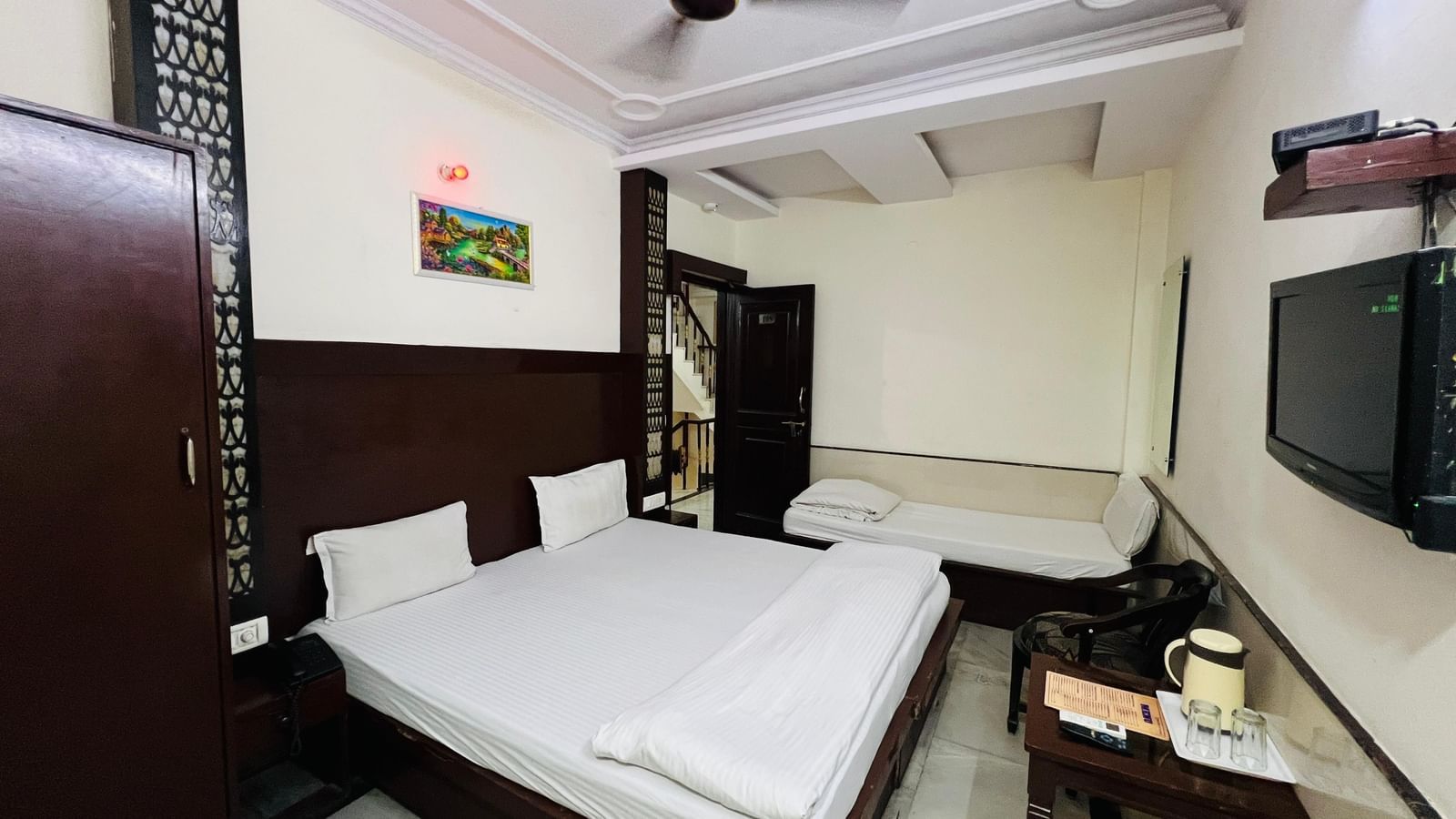 A hotel room with a spacious bed, a sofa, and a wall-mounted TV, offering a comfortable and entertaining environment. | Super Deluxe Room | Hotel City Palace DX