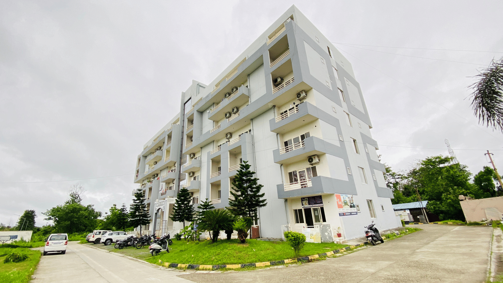 The facade of multi-storey Livbox, Rudrapur featuring the balconies, greenery, and a curved driveway in the foreground.