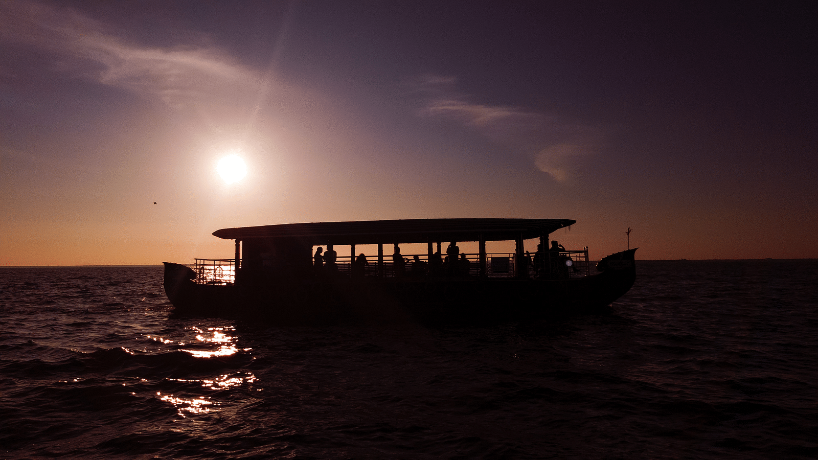 Silhouetted houseboat sailing on calm waters under the gentle light of the moon - Kumarakom