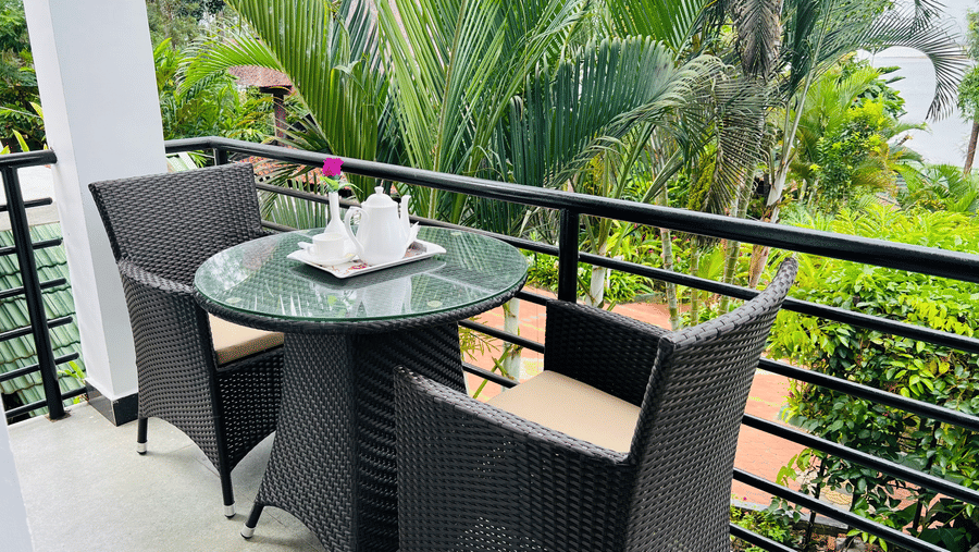 Image of a balcony with a chair and a table surrounded by trees on the side at Coorg Jungle Camp Backwater Resort, Kushalnagar.