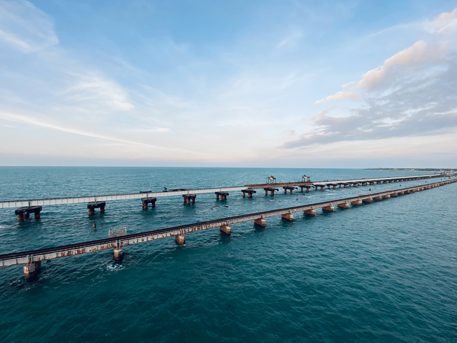 A serene coastal view featuring a long railway bridge stretching across calm blue waters beneath a soft pastel sky, capturing the quiet beauty of a seaside horizon.