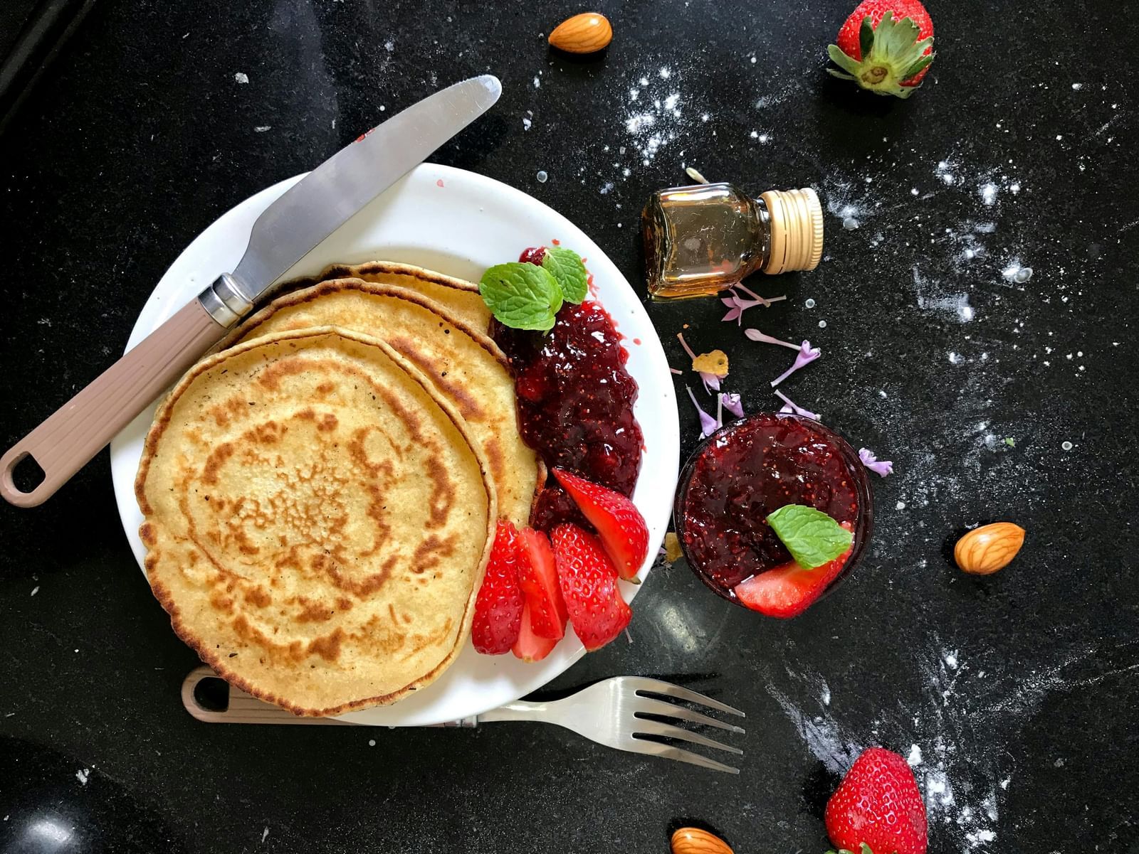 A colourful dish of food, possibly a pancake or omelette garnished with vegetables, placed on a white plate with cutlery.