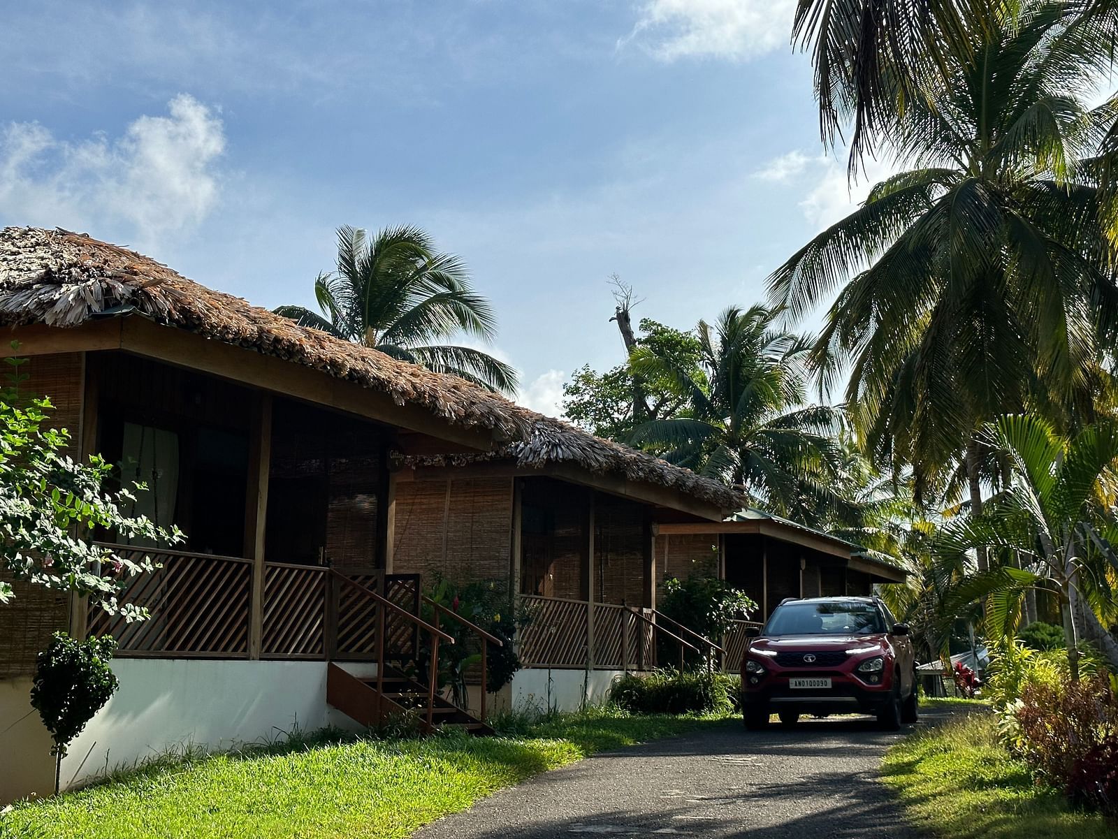 A charming resort building with a thatched roof, surrounded by lush green grass and palm trees under a bright sky.
