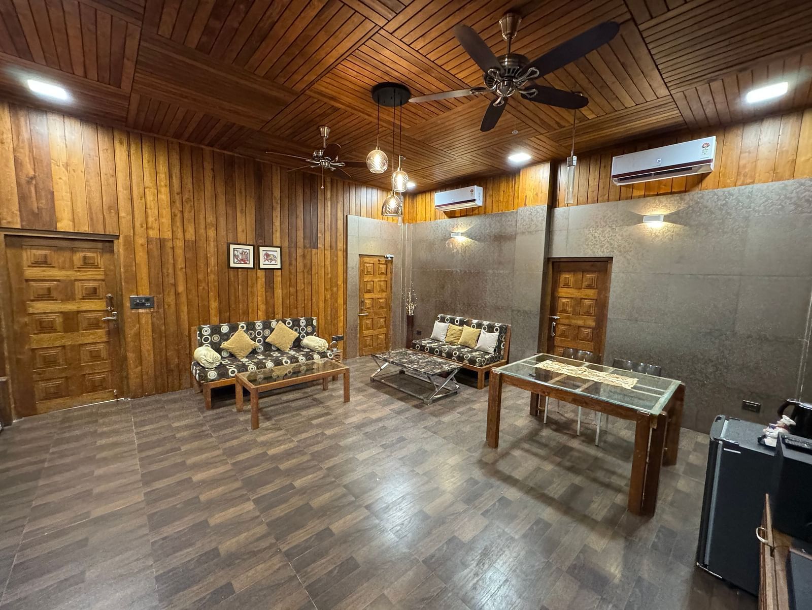 A wide-angle view of a rustic living area with wooden walls and ceiling, a patterned sofa, and a wooden coffee table.