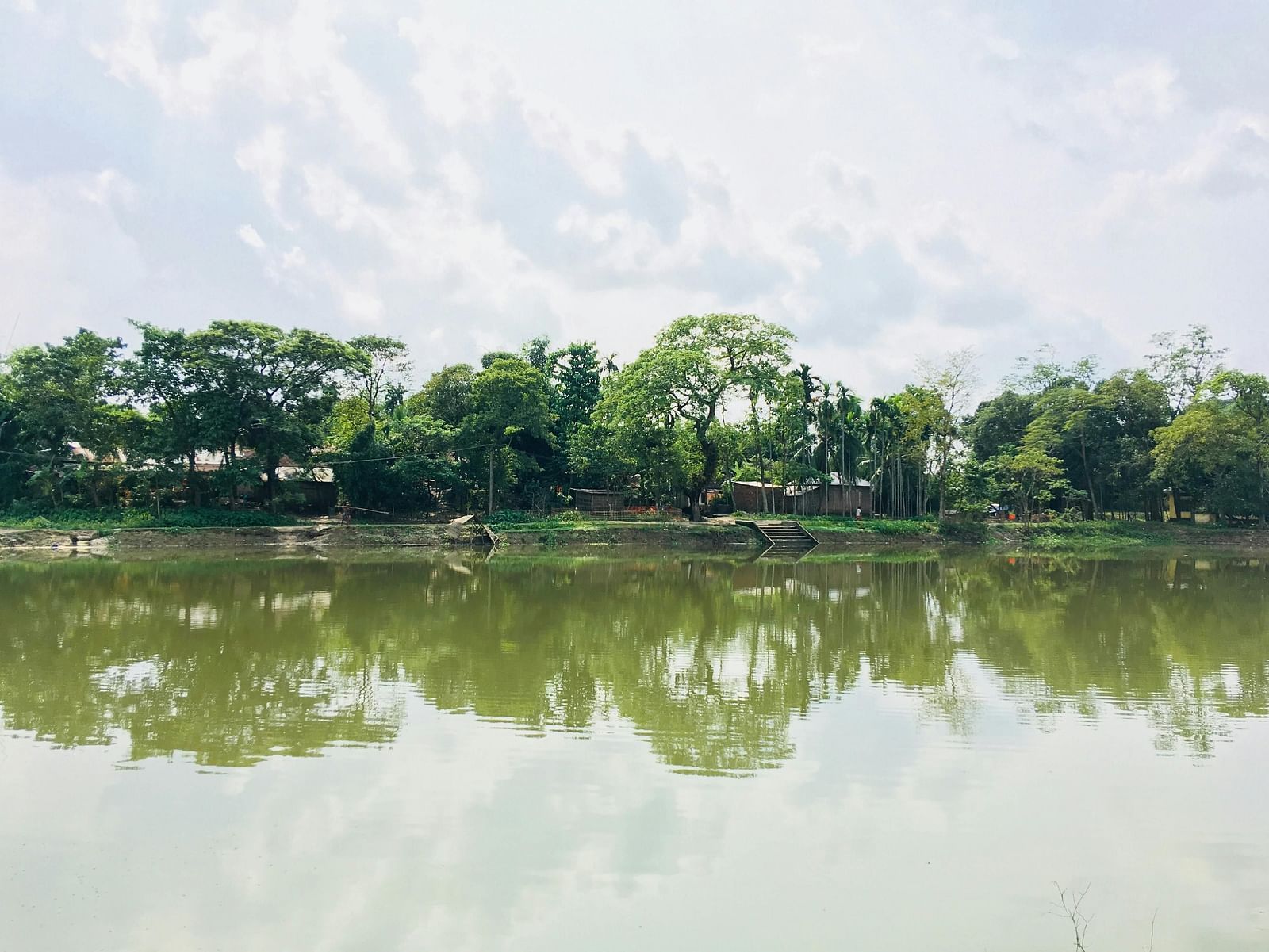 A lake with trees on the side, reflecting in the water along with the cloudy sky