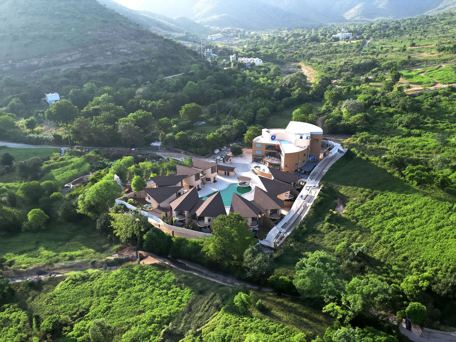 An aerial view of The Qualia Resort Club & Brewery, Udaipur surrounded by lush greenery and hills.