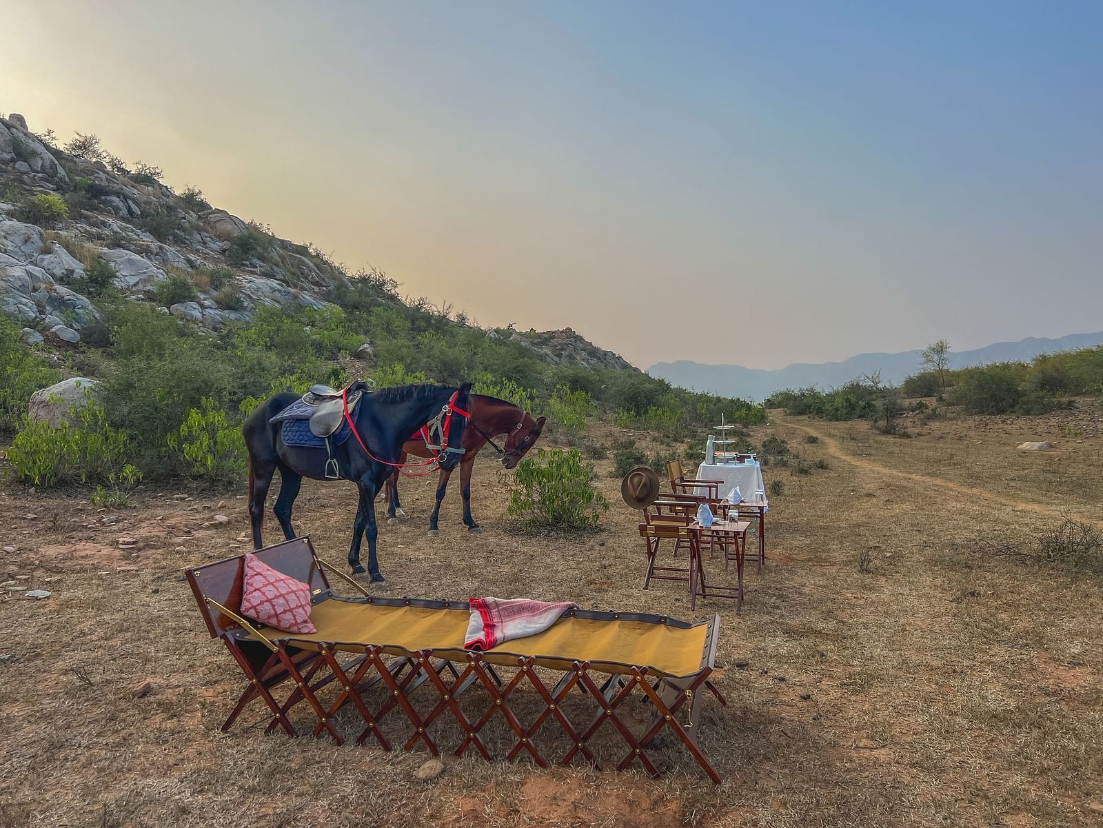 An image of two horses near a seating arrangement with mountains in the background - Utsav Camp Sariska