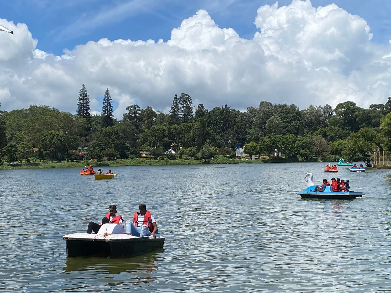 A beautiful scenery at the Yercaud Lake with several tourists paddle-boating under a bright blue sky with clearly-defined clouds in the background.