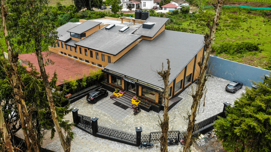High-angle view of a contemporary orange and grey building with a paved courtyard and surrounding greenery at Trident The Boutique Hotel, Ooty.