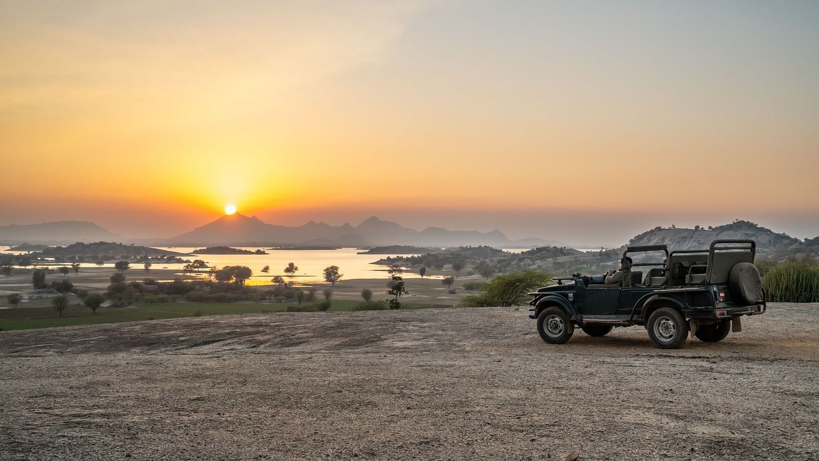 A jeep parked before a mountain with view of the sunrise.