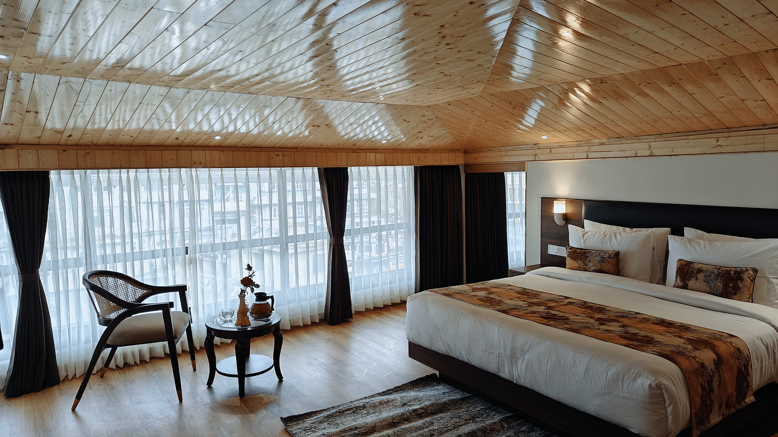 A hotel room featuring a neatly made bed with white linens and a patterned runner, accompanied by a chair and a small table beside it - Sumitel JB Park, Darjeeling