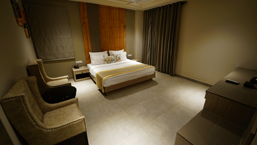 Wide angle view of a room at Five Elements Hotel with a king bed, lounge chair, dark curtains, and warm golden ambient lighting.