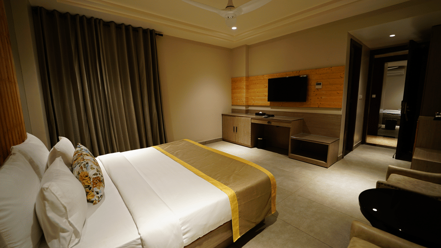 View of a room at Five Elements Hotel with a king bed, wall-mounted TV, dark curtains, wooden panelling, and warm ambient lighting.
