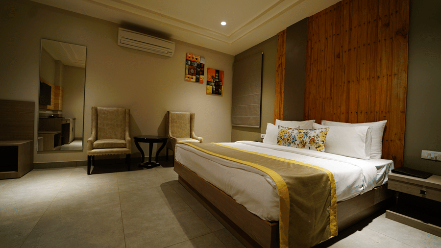 Side view of a room at Five Elements Hotel with a king bed, yellow accent runner, wooden wall panel, armchair, and warm ambient lighting.