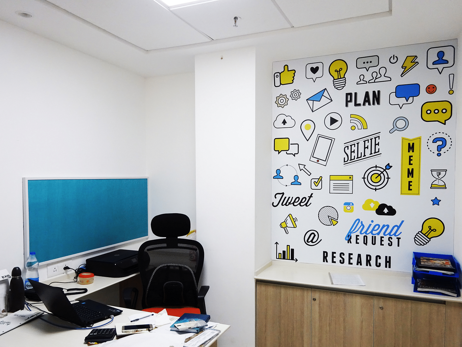 An office room with desk space, chair and a wall full of illustrations in the background.
