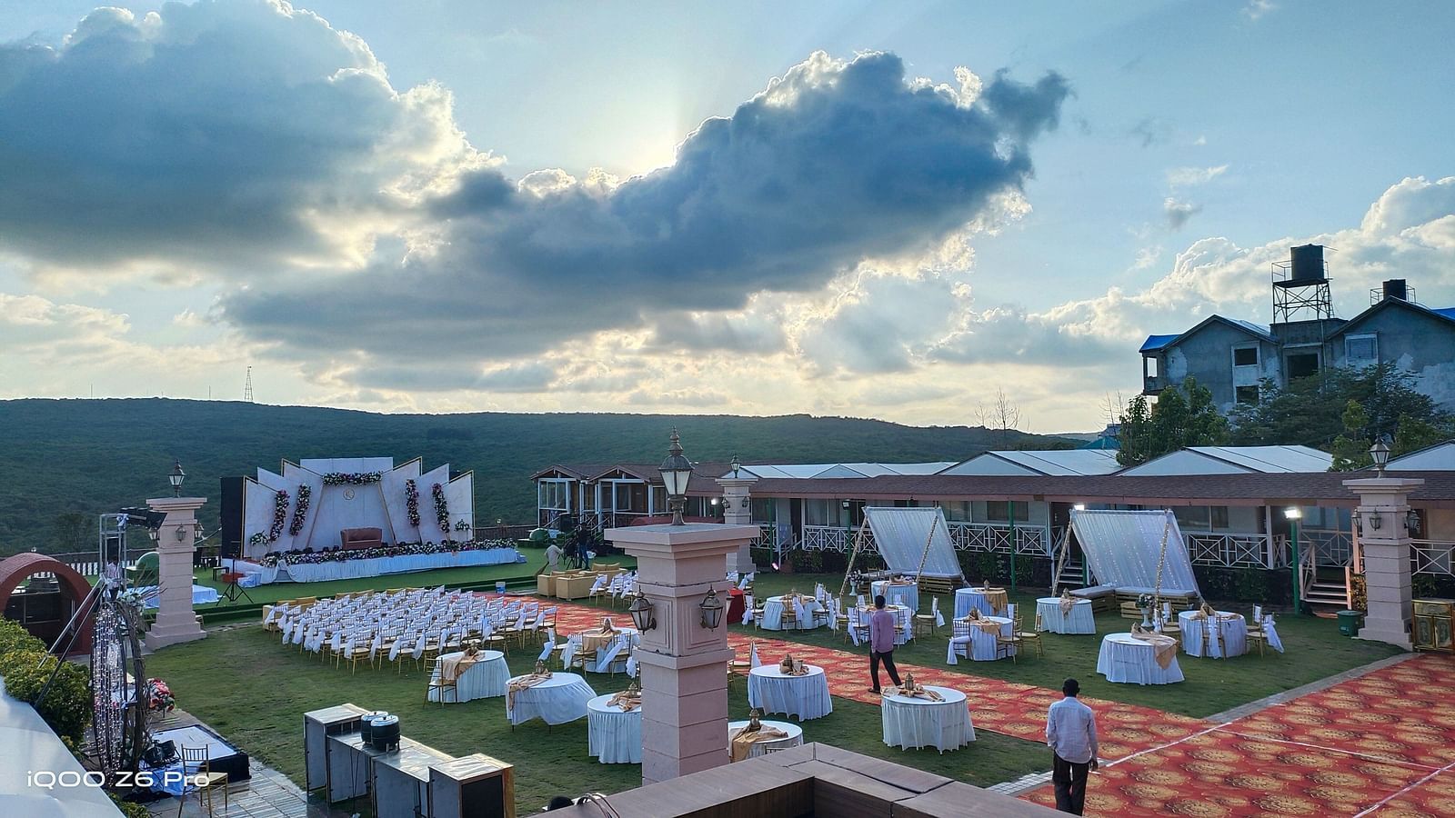 An outdoor wedding venue at dusk. Tents and decorations are set up on a sprawling landscape under a cloudy sky, suggesting a large celebration - The Grand Legacy Resort and Spa