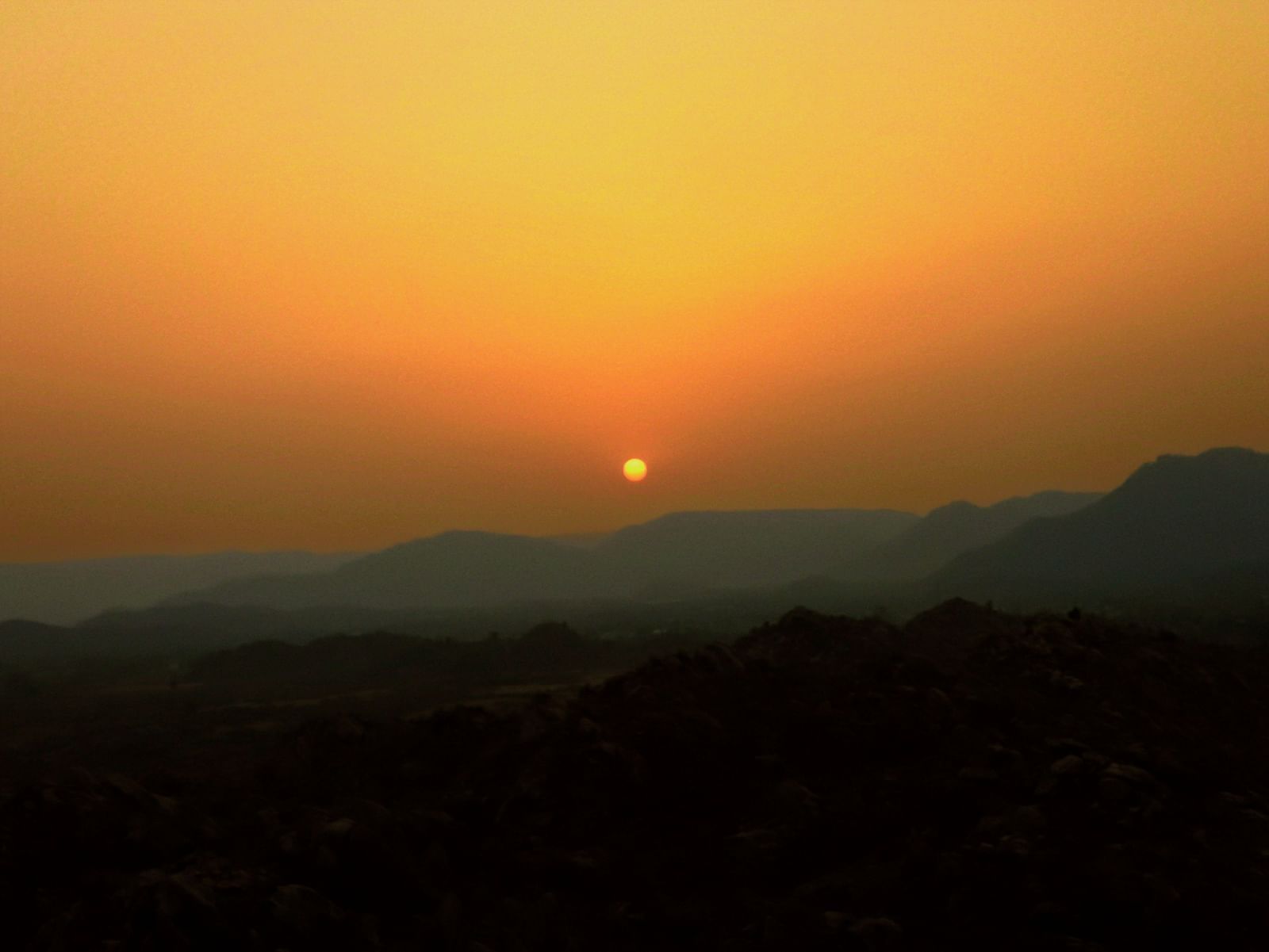 Sunset over rolling hills and mountain silhouettes in the wilderness.