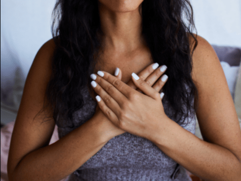 A woman placing her hands over her heart in a gesture of gratitude or calm.