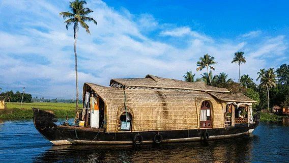A traditional Kerala houseboat navigating a body of water with palm trees along the shore.