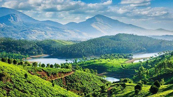 A panoramic view of rolling green hills, possibly tea plantations, under a blue sky with some clouds.