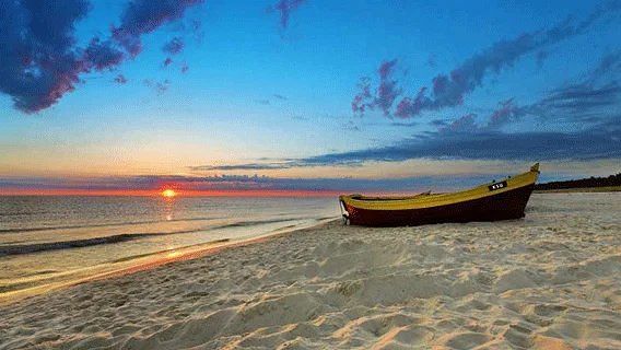A colorful sunset over a beach with a fishing boat pulled onto the sand.